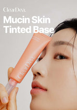 A close-up beauty shot of a woman holding a tube of ClearDea Mucin Skin Tinted Base against a light neutral background, with product text overlaid at the top.