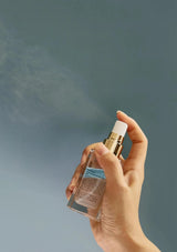 Hand holding a spray bottle with mist against a plain background