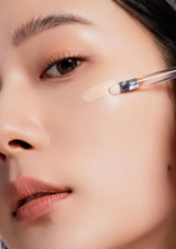 Close-up of a person applying concealer with a brush on their face.