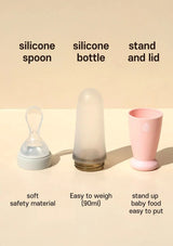 Baby feeding items including a silicone spoon, bottle, and cup on a beige background.