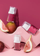 Three lip glosses on a pink surface with figs