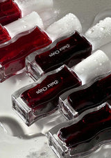 Close-up of red nail polish bottles with 'Dana Chans' branding on a textured surface.