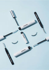 Cosmetically branded eyelash products including mascara and false eyelashes on a light blue background.