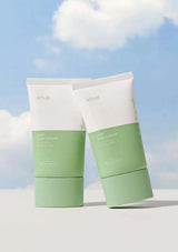 Two green and white skincare products on a white surface with a blue sky background