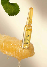 AIDA skincare ampoule with honeycomb and leaf on a gradient background
