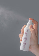 Hand holding a white spray bottle labeled 'KOPER' against a gray background
