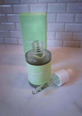 Green skincare bottle with dropper on a light surface