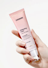 Hand holding a pink tube of COSNORI Whitening Dress Tone-Up Cream against a white background