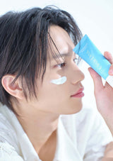 Person applying a skincare product to their face with a blue container.