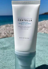 Skint004 Madagascar Centella sunscreen tube on a reflective surface with a beach background