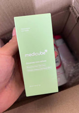 Green skincare serum bottle held by a hand with a brown background