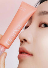 Person holding a 'ClearDea' skincare product near their face against a light background