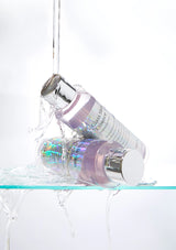 Two skincare bottles with iridescent cap designs hanging above a clear surface.
