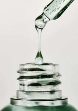 Close-up of a dropper bottle with liquid being dispensed into a glass container on a light gray background.