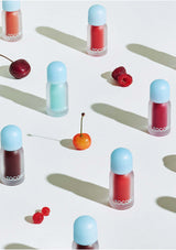 Tocoto lip gloss bottles with blue caps on a light background with cherries and raspberries.