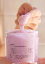 Pink shampoo jar with a fluffy pink substance being poured into it, against a blurred background.