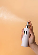 Hand holding a skincare bottle with a gold cap against a beige background
