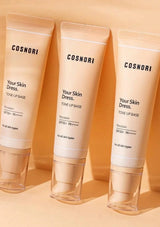 Three tubes of COSNORI 'Your Skin Dress' Tone Up Base on a peach background