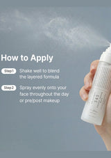 Hand holding a skincare spray bottle with application instructions on a gray background