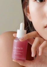Person holding a bottle of Arencia serum close to their face