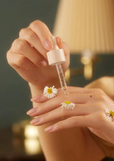 Hand holding a dropper with a small white flower, blurred background