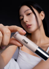 Woman holding a cosmetic product with 'Oliad' branding against a black background