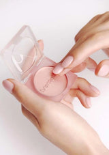 Hand holding a pink makeup product with a clear case on a light background