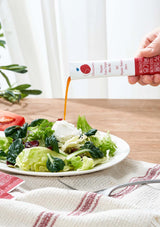Salad with a dressing being poured from a bottle on a wooden table.