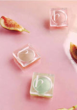 Clear square containers with 'b' logo on a pink surface with figs and a bowl.