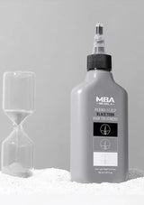 Bottle of MBA Derma Scalp Blackout hair treatment with an hourglass on a gray background