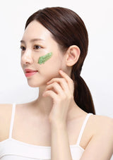 Woman with a green leaf product on her cheek against a white background