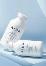 Two AIDA skincare bottles on a light blue background