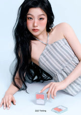 Woman with long black hair wearing a gray striped dress, sitting on a light blue background.
