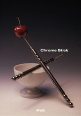 A pair of metallic chrome sticks with decorative ball accents and a small stem, crossed over a white pedestal bowl on a dark gradient background. The text 'Chrome Stick' and 'Aheb' are visible on the image.