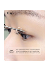 Close-up of a person's eye with an eyebrow curling tool applied to the eyebrow, with text and arrow indicating the curling motion. Brand name Aheb is visible at the top left.