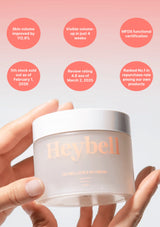 Hand holding a Heybell product container with text highlighting features on a pink background