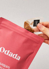 Person opening a red Odada package with a small packet of food.