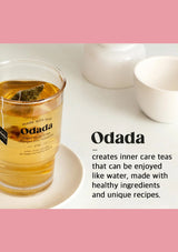 Glass of Odada tea with a tea bag, surrounded by white teacups on a light surface.
