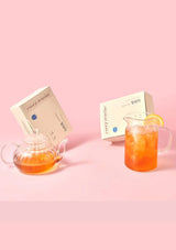 Tea set with a teapot, glass, and boxes on a pink background