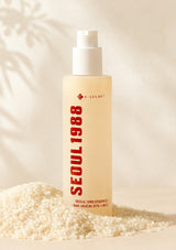 Skincare bottle labeled 'Seoul 1988' on a neutral background with rice grains.