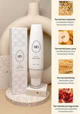 White skincare product with packaging on a neutral background, featuring images of ingredients on the side.