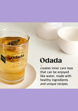 Glass of Odada tea with a tea bag on a white surface, featuring text about the brand and its teas.