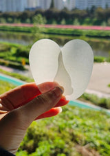Hand holding two white heart-shaped objects with a blurred green outdoor background
