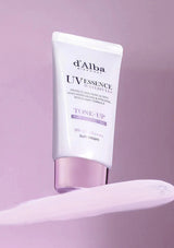 Tube of d'Alba UV Essence Waterlily Tone-Up sun cream on a pink background