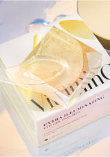A box of K-Secret Extra Illuminating Eye Gel Patches with Vitamin C, showing the product name and patches in yellow color with a golden spatula.