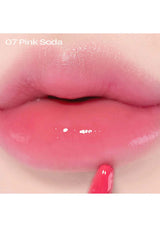 Close-up of lips with pink lip gloss labeled '07 Pink Soda' on a white background