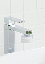 A modern chrome single-handle bathroom faucet with a clear cylindrical filter attachment, mounted against a white tiled wall.