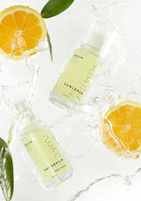 Two skincare serum bottles labeled 'SU' with orange slices and leaves on a white background