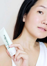 Woman applying a white stick product to her arm with a neutral background
