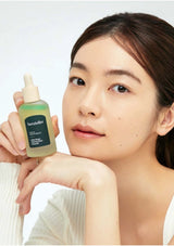 Woman holding a bottle of skincare product with a plain background